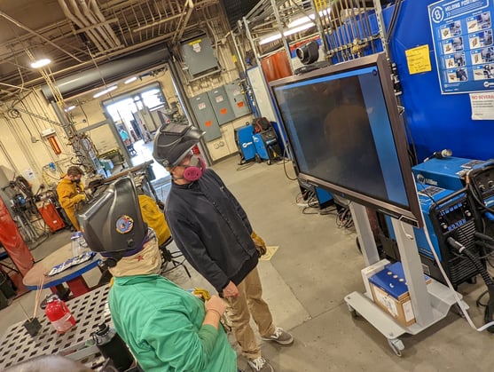 Two students viewing a weld from a large display screen in the welding classroom